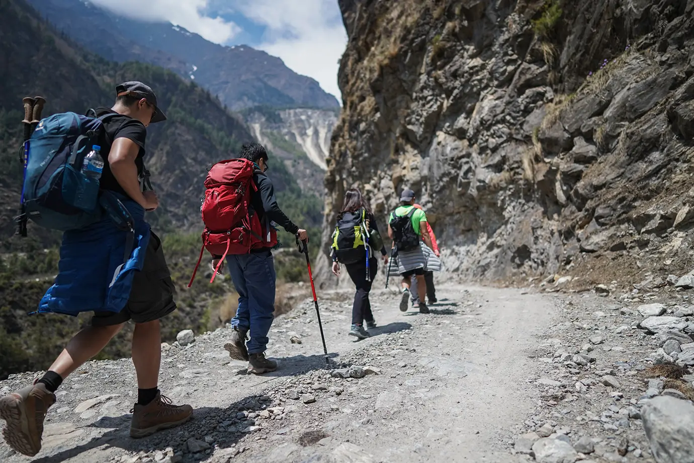 Trekkers hiking rocky trail in Manang Nepal with backpacks and trekking poles in mountain terrain