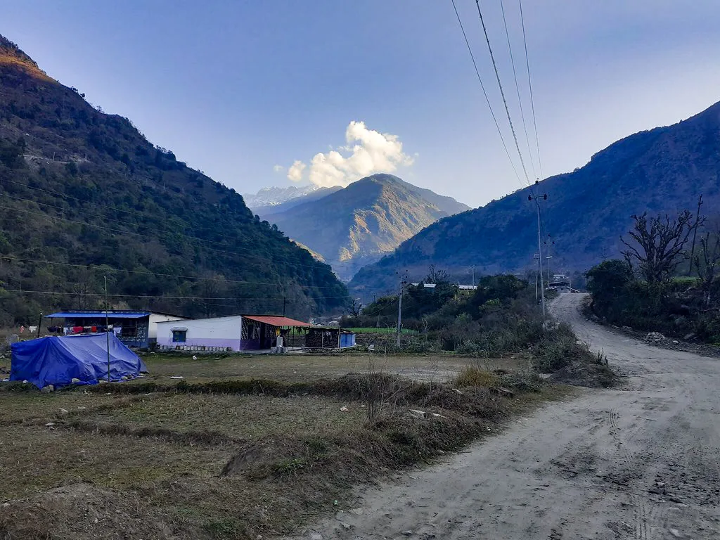 A rural mountain village with simple houses and a blue tarp sits beside a dirt road in a valley of the Luxury Annapurna Circuit Trek.