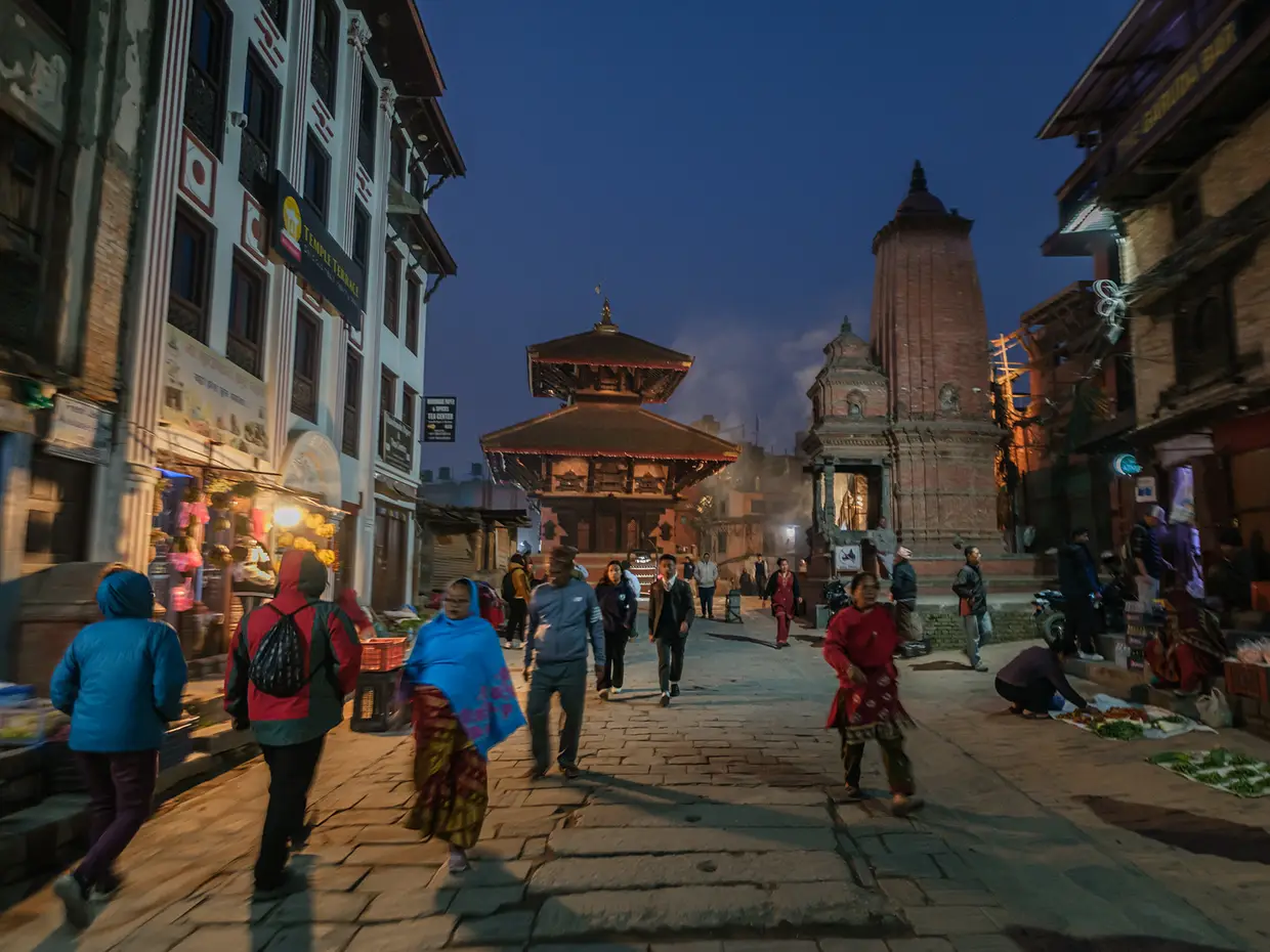 People walk through a stone paved square in Bhaktapur at dusk. This historic walk is a beautiful part of a Kathmandu Luxury Experience.