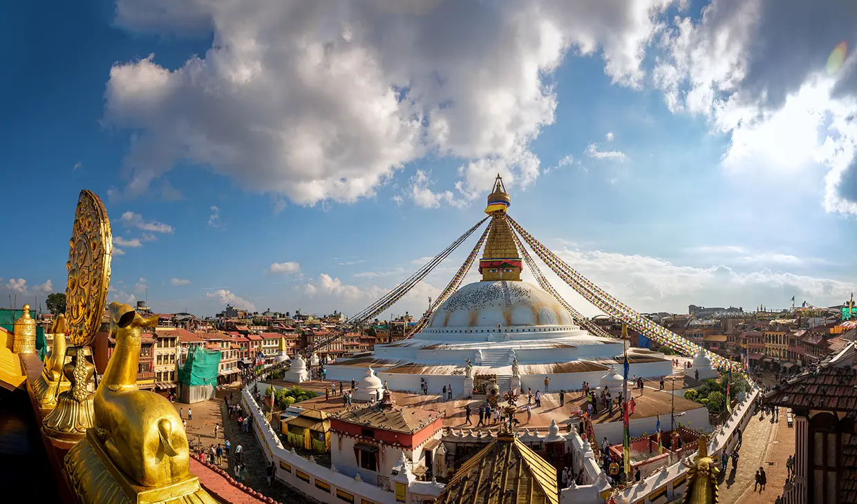 The white dome of Boudhanath Stupa sits under a blue sky with prayer flags. This landmark is a key stop on your Nepal Luxury Tour Itinerary.
