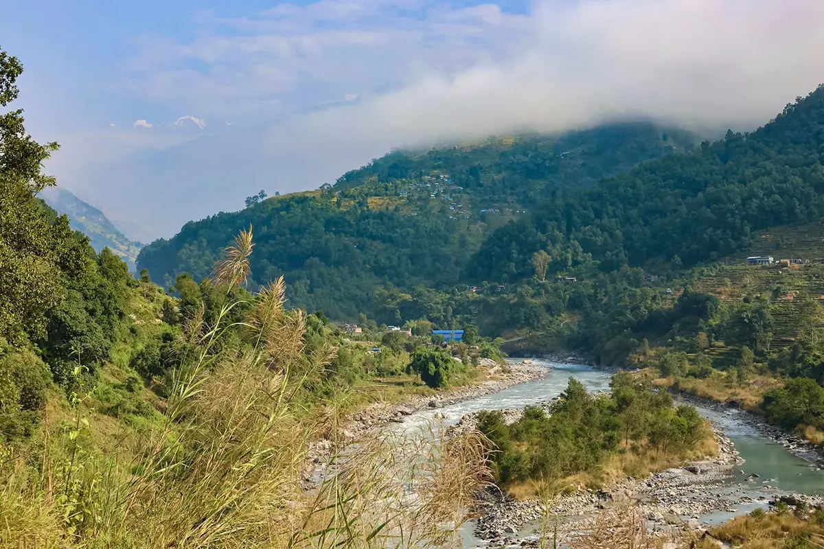 The Budhi Gandaki River flows through a lush green valley with mist covered hills and terraced fields during a Luxury Manaslu Trek in Nepal.