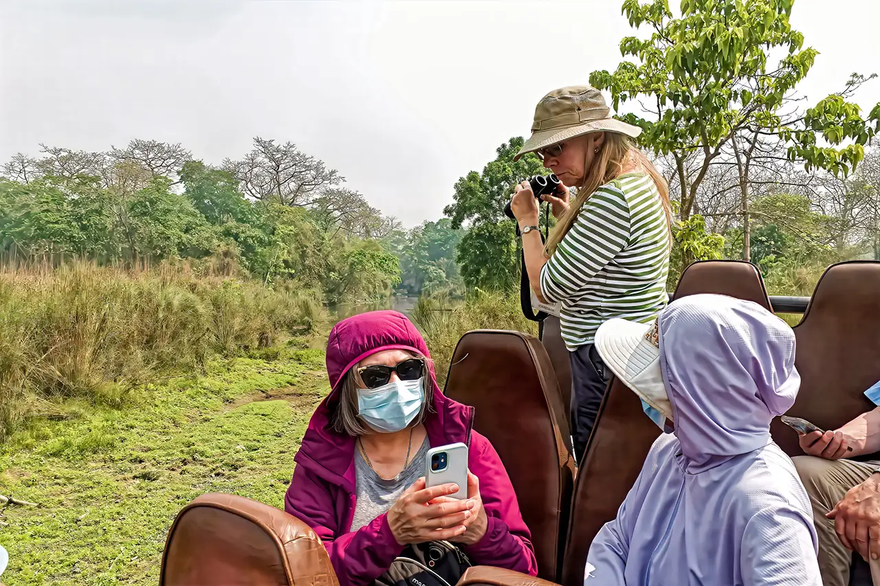 Tourists enjoy a jungle safari at Chitwan National Park, with travelers using binoculars and mobile phones while viewing the forest and wetlands.