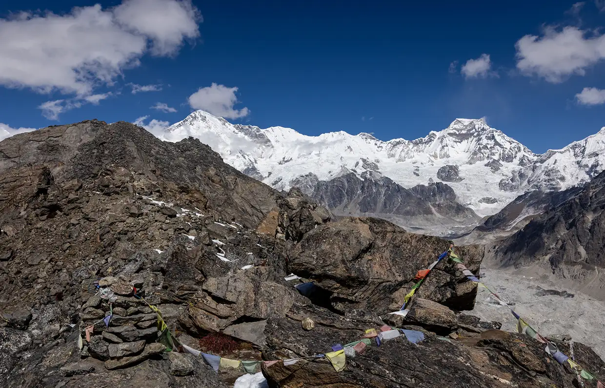 A rocky mountain ridge with colorful prayer flags overlooks a massive glacier and the snow-capped Cho Oyu range during a Luxury Everest Base Camp & Gokyo Lakes Trek.