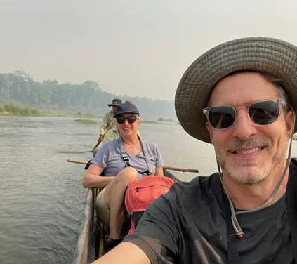 A smiling couple takes a selfie during a private dugout canoe ride on a river in Chitwan National Park, a central part of their Luxury Nepal Honeymoon Tour.