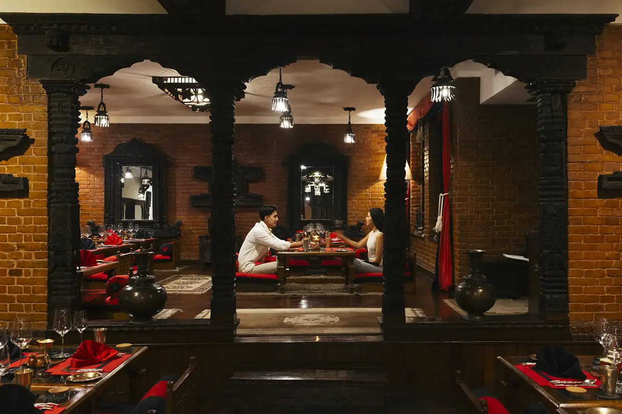 A couple enjoys a traditional multi-course meal at Dwarika's Hotel in Kathmandu during a Luxury Nepal Honeymoon Tour. The room showcases historic Newari architecture and woodwork.