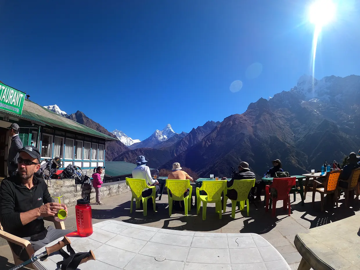 Travelers sit at an outdoor restaurant terrace facing snowy Himalayan peaks under a bright sun. This scenic mountain breakfast often complements a Luxury Nepal Honeymoon Tour.