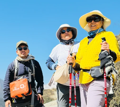 Three hikers wearing sun protection and carrying trekking poles stand on a mountain trail with a first aid kit during a Luxury Everest Panorama Trek.