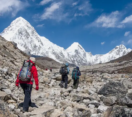 Luxury Everest Three Passes Trek hikers cross a rocky Himalayan trail with snow-covered peaks and clear blue skies in the Everest region.