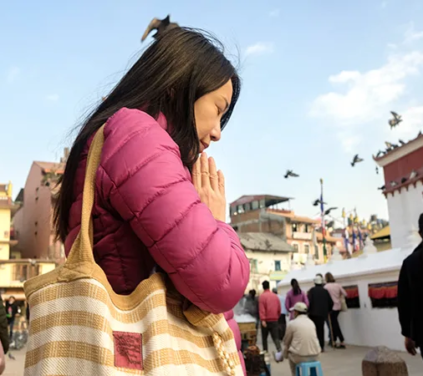 Uma mulher com uma jaqueta rosa reza no Stupa de Boudhanath, no Nepal. Essa experiência espiritual faz parte de um pacote turístico de luxo que abrange Kathmandu e Pokhara.