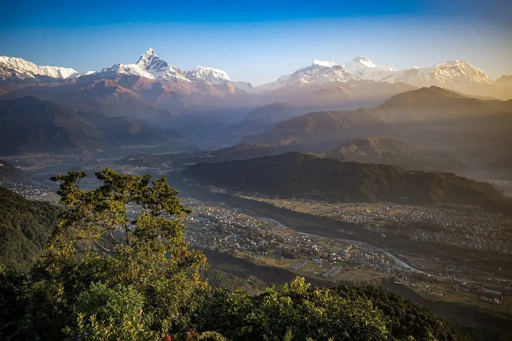 A stunning golden sunrise illuminates the snow-capped Annapurna mountain range and Machhapuchhre peak above Pokhara valley, a highlight of a Nepal Luxury Tour from India.