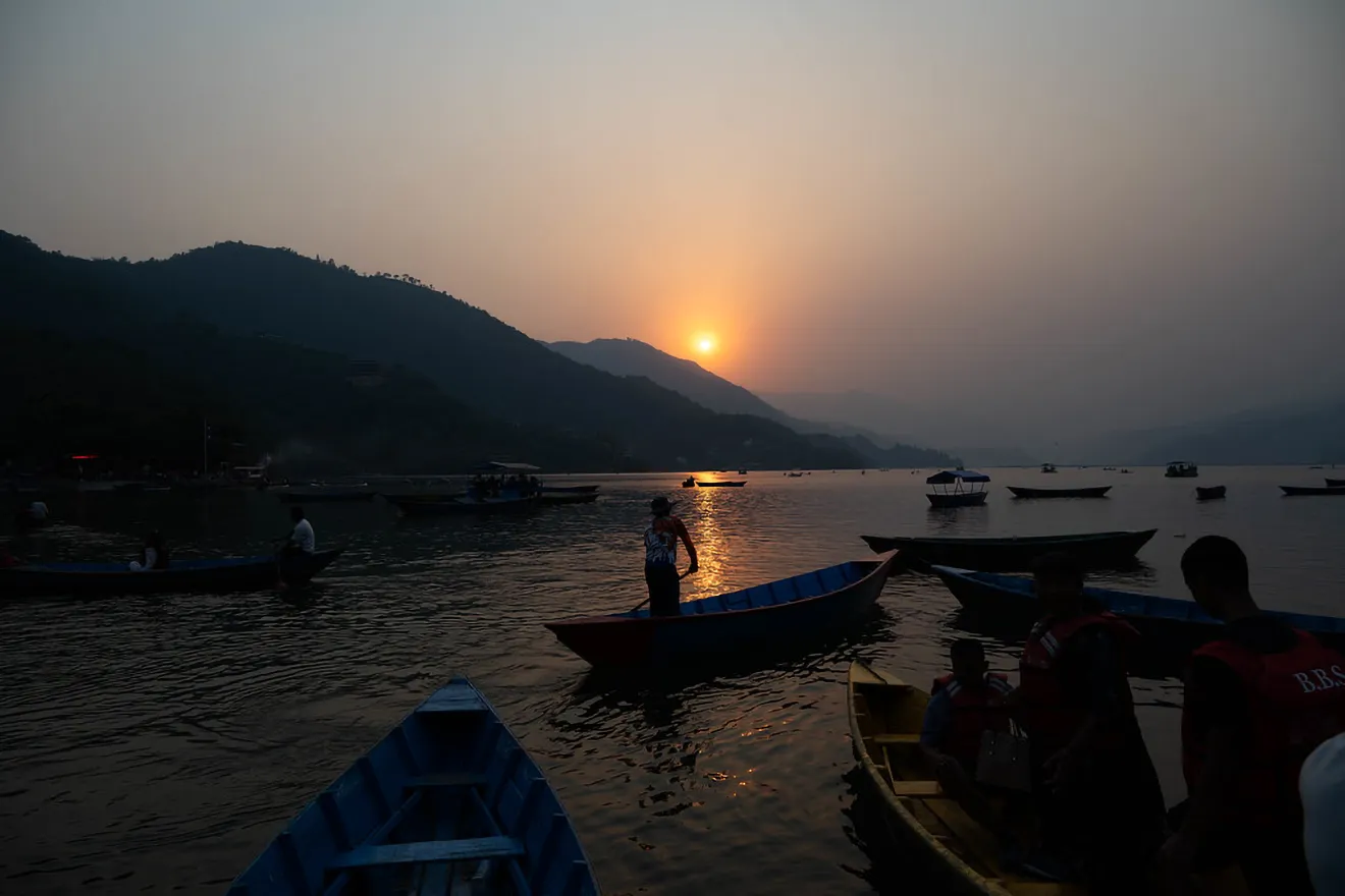 Wooden boats float on Phewa Lake during a golden sunset behind distant mountains. This scenic boat ride is a relaxing highlight of a Nepal Luxury Tour Itinerary.