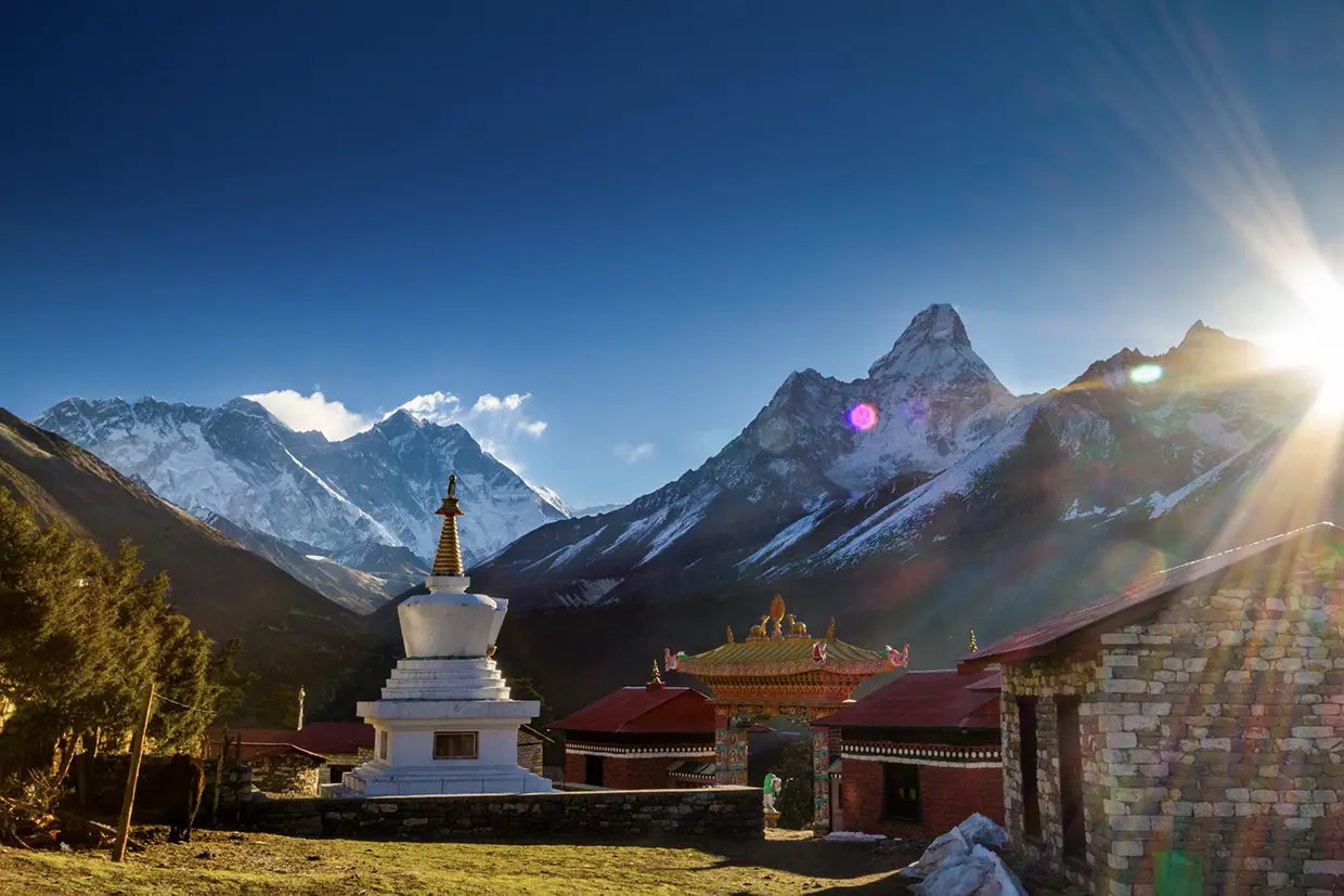 A white Buddhist stupa and the stone buildings of Tengboche Monastery sit before the sunlit peaks of Ama Dablam during a Luxury Everest Base Camp & Gokyo Lakes Trek.