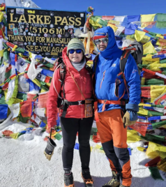 Trekkers standing at Larke La Pass surrounded by colorful prayer flags during the Manaslu Circuit Trek in Nepal.