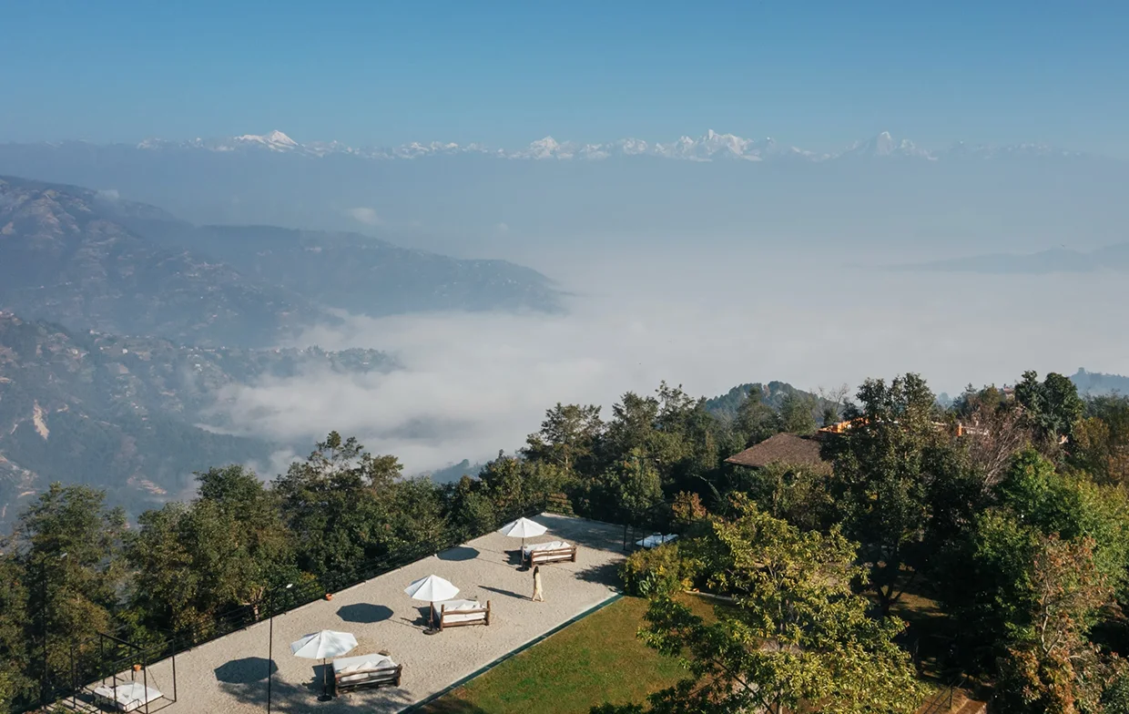 An aerial view of a mountain resort terrace with modern cabanas above the clouds, overlooking snow-capped Himalayan peaks, a key experience on our Luxury Nepal Honeymoon Tour.