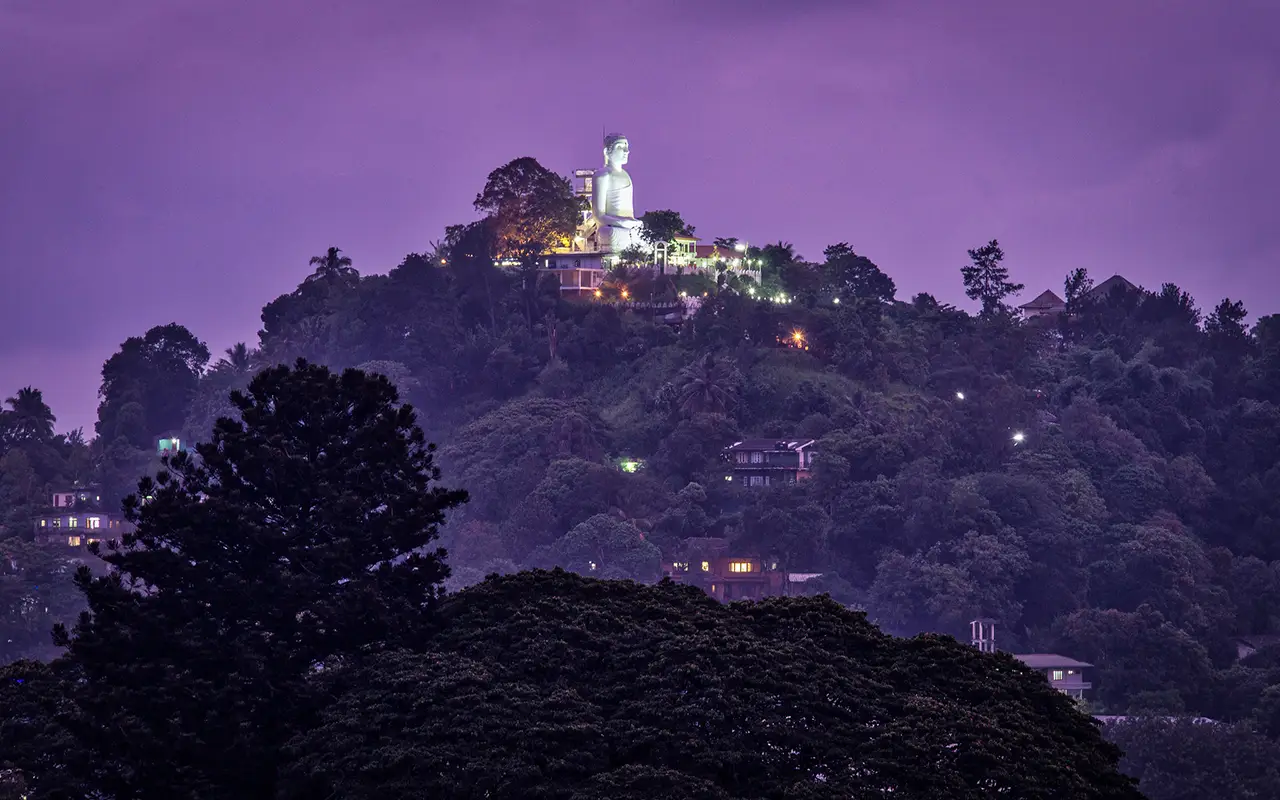 Sri Lanka Itinerary features the illuminated giant Buddha statue overlooking the hill-country city of Kandy at dusk.