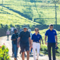 Pekoe Trail features a group of hikers walking along a dirt path through lush green tea plantations in Sri Lanka.