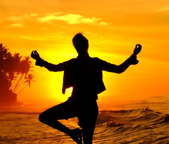 Ayurveda in Sri Lanka is complemented by a person practicing yoga in silhouette against a golden sunset on a tropical beach.