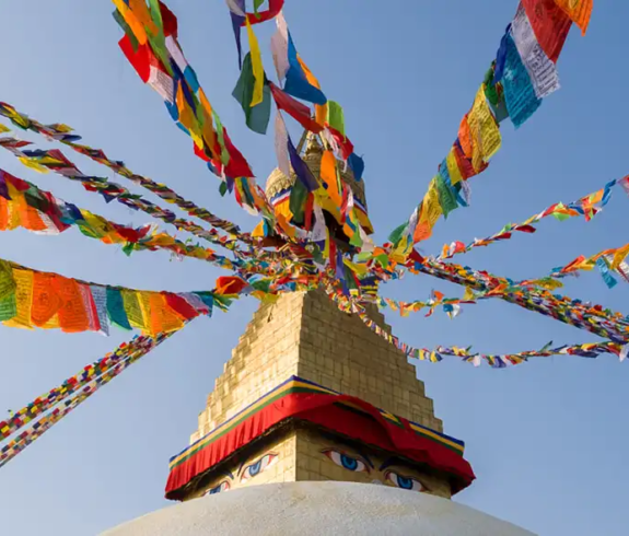 Best Time to Visit Nepal features colorful prayer flags radiating from the top of the sacred Boudhanath Stupa against a clear blue sky.