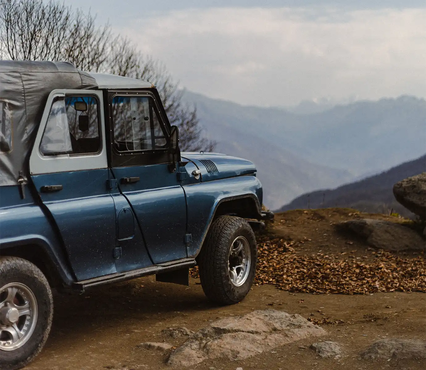 A blue off-road 4x4 vehicle parked on a dirt mountain trail against hazy peaks, illustrating transport rental expenses for Georgia Travel Cost.