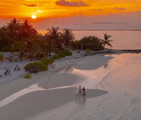 A couple walking along a sandy shoreline during a golden sunset featured in an article exploring Is a Maldives All-Inclusive Luxury Resort Holiday Worth It?