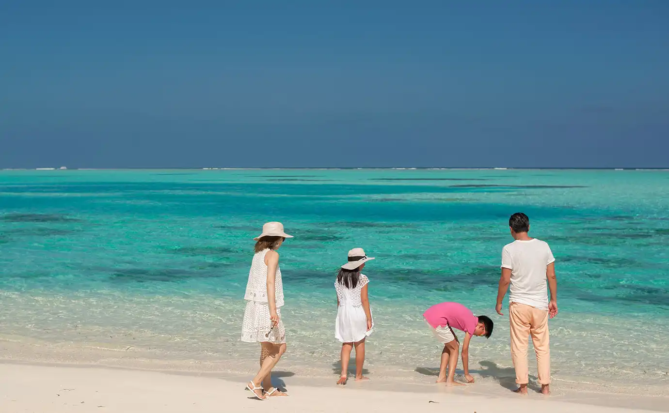 A family of four strolling along the shoreline of a white sand beach featured in an article asking Is a Maldives All-Inclusive Luxury Resort Holiday Worth It?