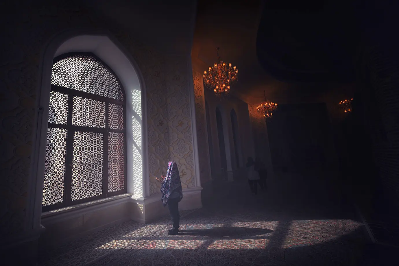 A person standing in prayer near an ornate latticed window as sunlight streams onto the carpeted floor inside a Baku mosque featured in a travel guide on 10 Essential Things to Know Before Visiting Azerbaijan.