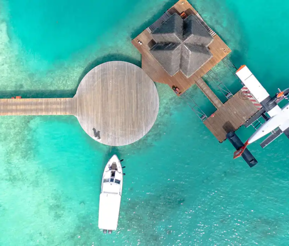 Bird's-eye view of a seaplane and boat docked at a wooden island jetty in clear turquoise waters featured in a Maldives Travel Guide for First-Timers.