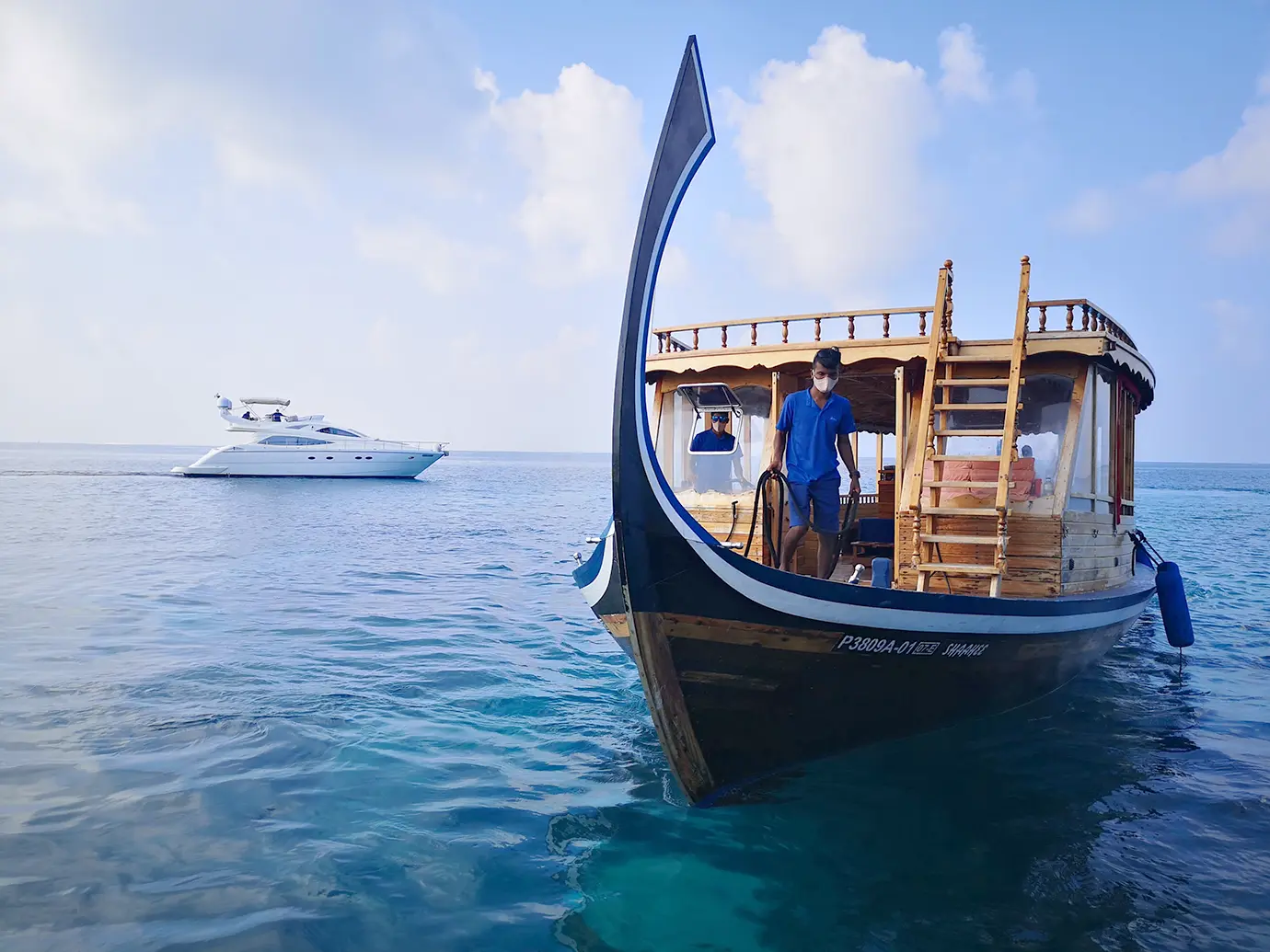 A traditional handcrafted wooden dhoni boat floating near a modern white luxury yacht on turquoise sea waters featured in a guide on How to Plan a Maldives Luxury Honeymoon on an Affordable Budget.