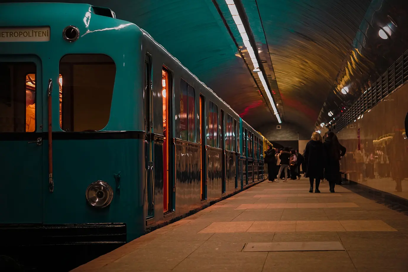 A vintage turquoise Baku Metro train standing at an underground station platform with passengers waiting under soft lighting featured in a travel guide on How Much Does a Trip to Azerbaijan Cost?