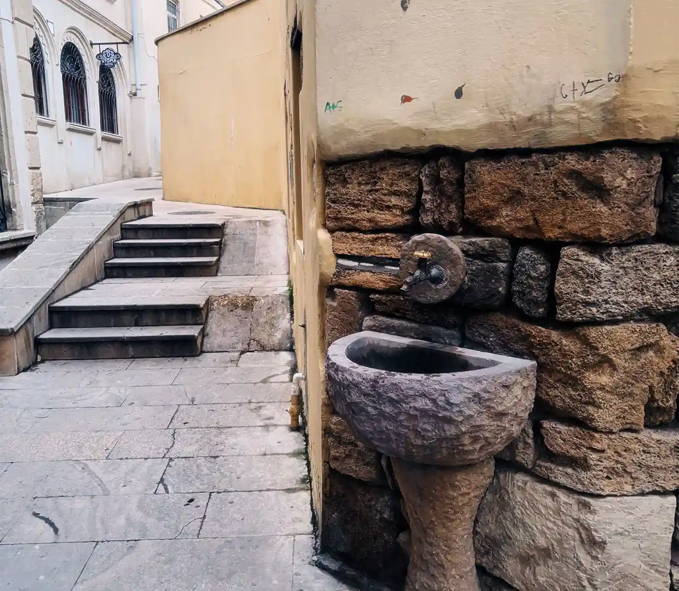 A traditional carved stone drinking fountain and stone basin attached to a masonry wall in an Old City alley featured in a travel guide on How Much Does a Trip to Azerbaijan Cost?