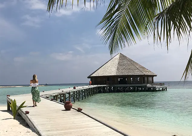 Bird's-eye view of a seaplane and boat docked at a wooden island jetty in clear turquoise waters featured in a Maldives Travel Guide for First-Timers.