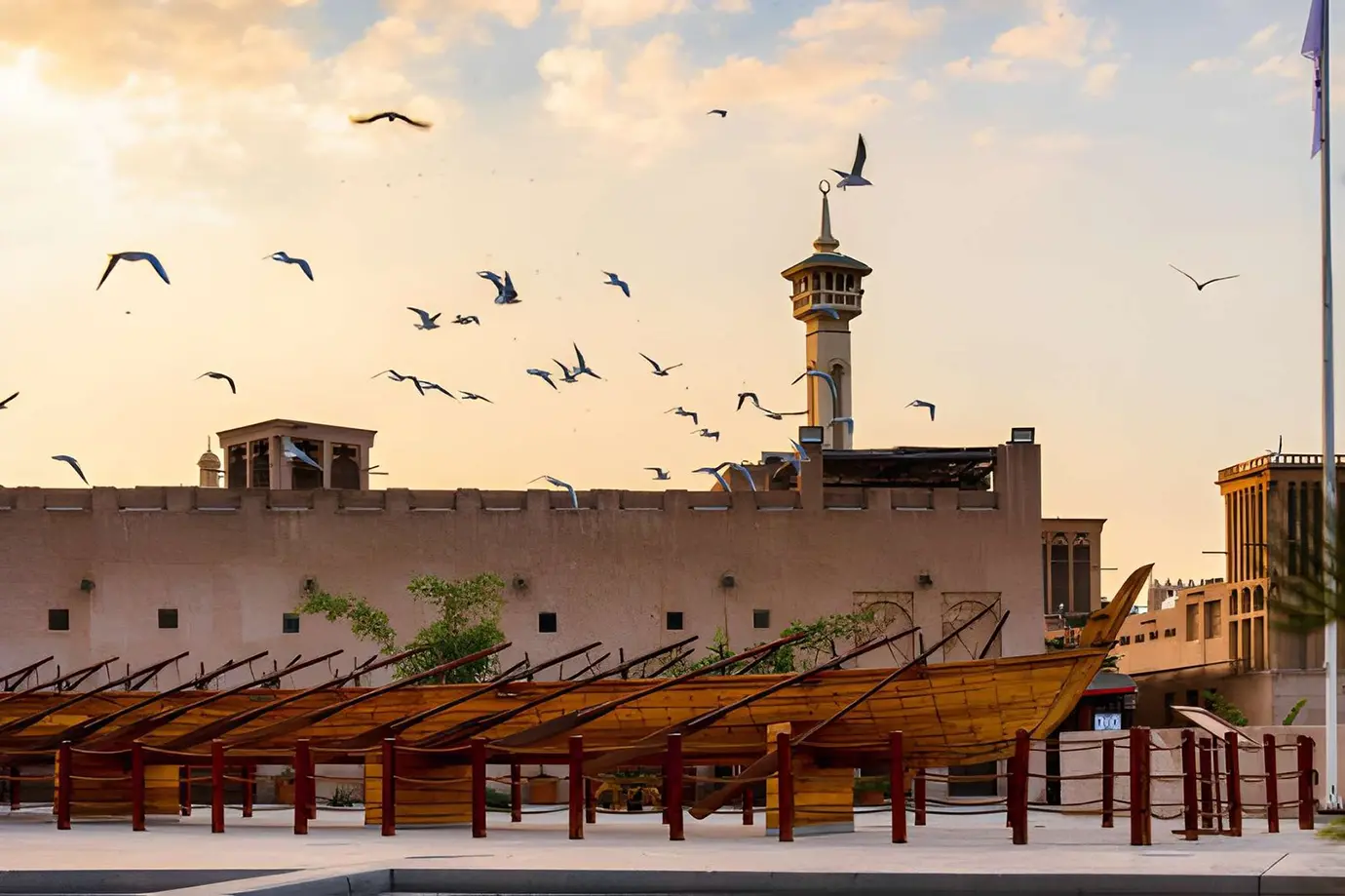A traditional wooden rowing vessel displayed in front of wind towers and a minaret in the Al Fahidi Historical Neighbourhood, representing cultural Things to Do in Dubai.
