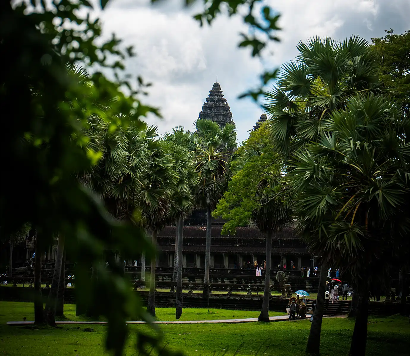 The stone spire of Angkor Wat rising above dense green palm trees and vibrant lawns featured in a travel guide on Cambodia Itinerary.