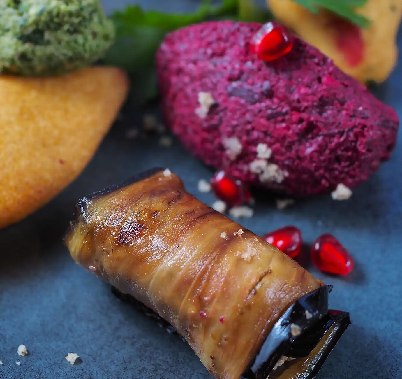A pan-fried eggplant roll stuffed with spiced walnut paste alongside vibrant beet pkhali garnished with pomegranate seeds, illustrating classic starters for a Georgian Food Guide.