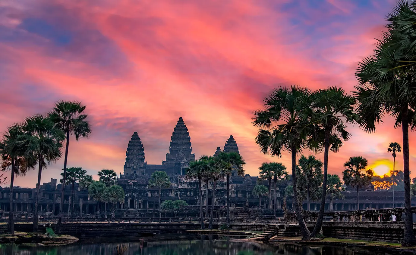 A stunning pink and orange sunset sky illuminating the ancient central stone spires of Angkor Wat featured in a travel guide on the Best Time to Visit Cambodia.