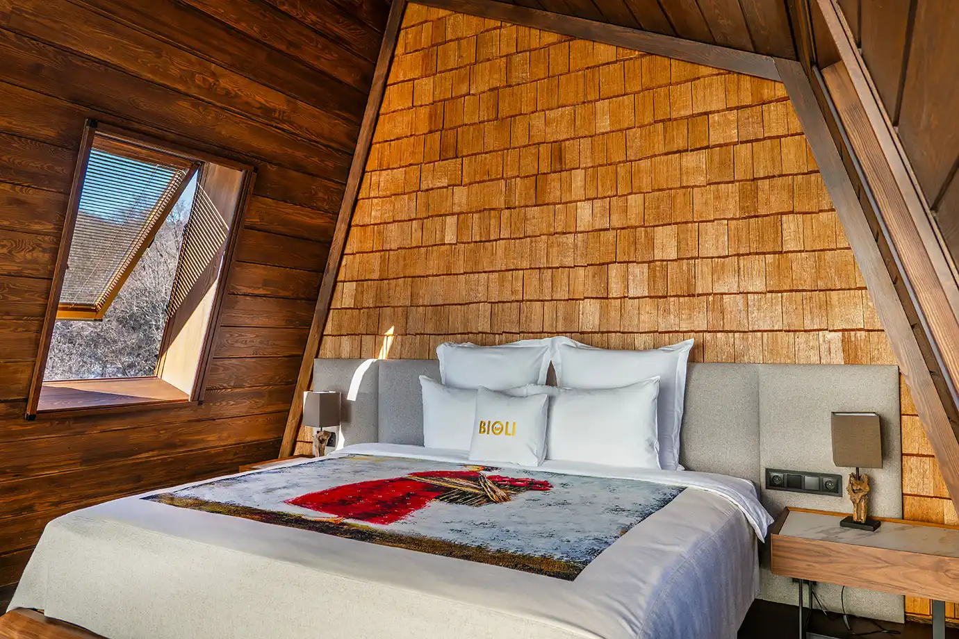 A luxury cottage bedroom featuring a wooden vaulted ceiling, skylight window, and plush king bed, highlighting upscale lodging options that increase overall Georgia Travel Cost.