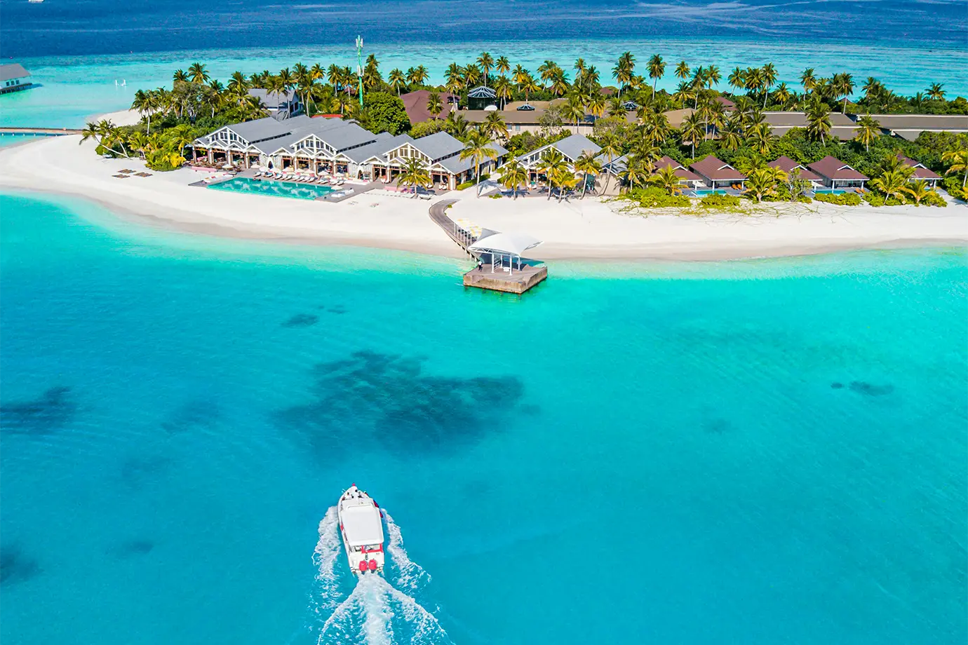 A white speedboat cruising through clear turquoise waters toward a tropical resort island with beach villas featured in a guide on How to Plan a Maldives Luxury Honeymoon on an Affordable Budget.