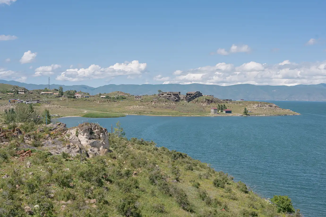 Deep blue waters of Lake Sevan stretching along grassy, rocky shorelines under a bright summer sky in Armenia featured in a travel guide on Best Places to Visit in Armenia.