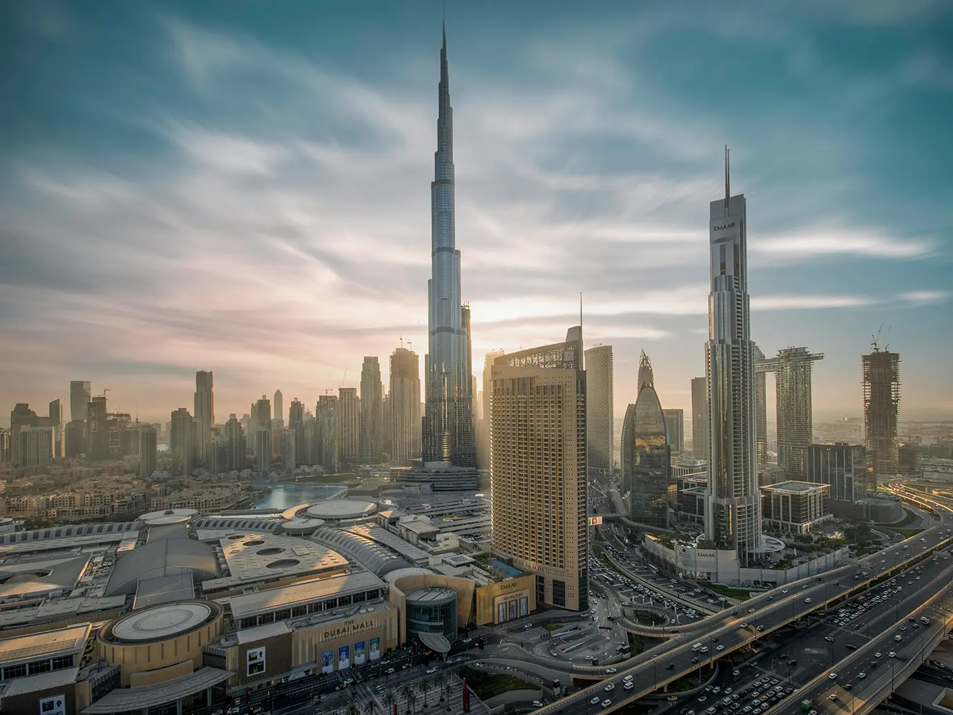 An elevated cityscape photograph showing the Burj Khalifa towering over The Dubai Mall and surrounding skyscrapers, a must-see attraction when looking for Things to Do in Dubai.