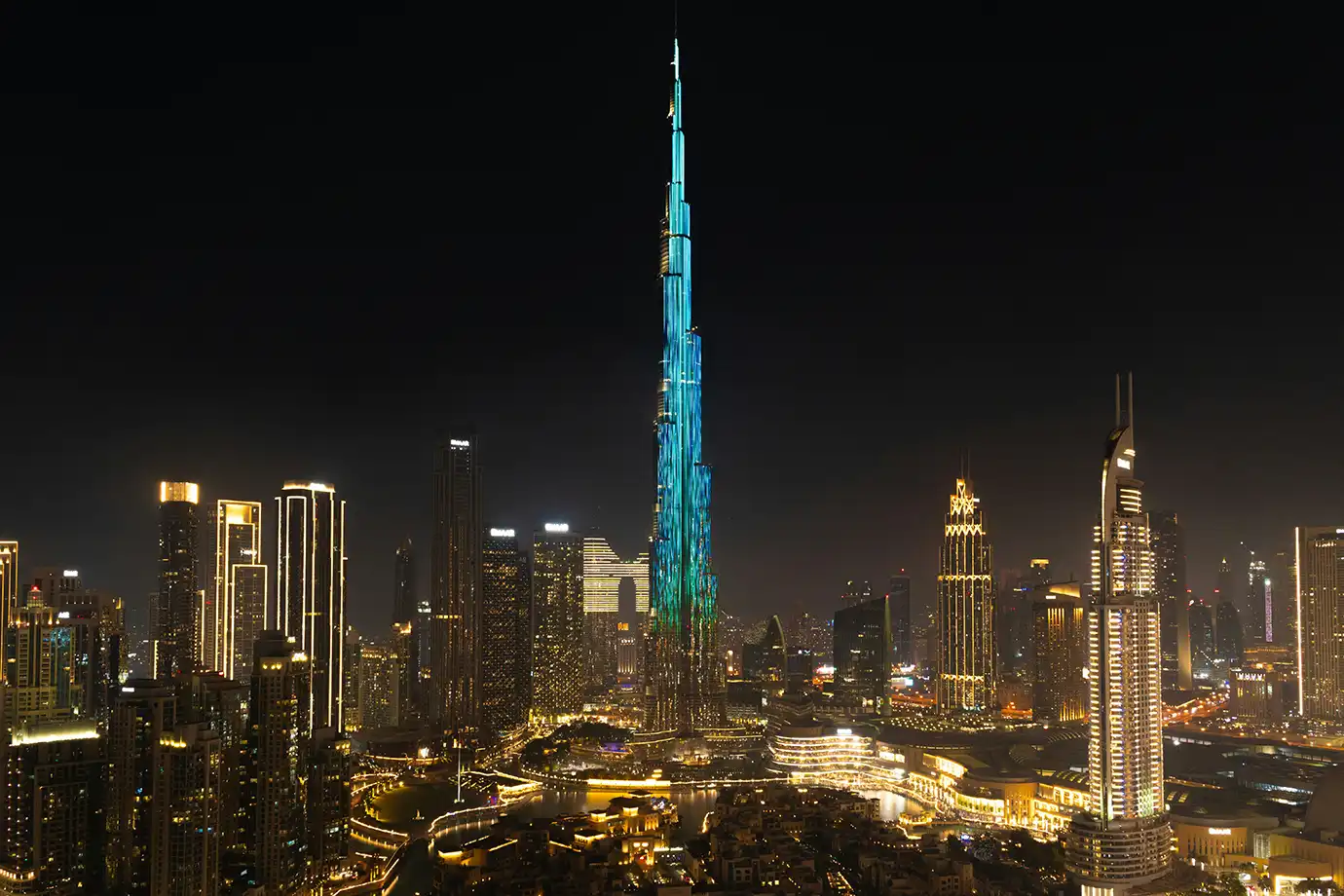 The Burj Khalifa skyscraper glowing with vibrant blue-green LED lights above the illuminated Downtown Dubai skyline at night, featured in Best Time to Visit Dubai.