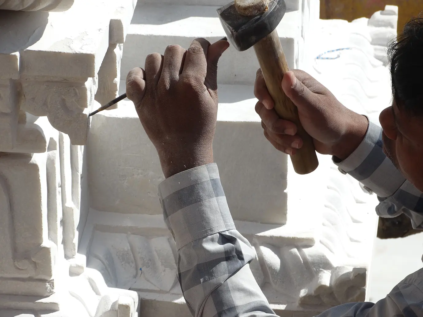 An artisan carefully sculpting fine details onto a white stone structure using a small chisel and wooden hammer featured in a guide on Things to Do in Siem Reap Beyond Angkor Wat.