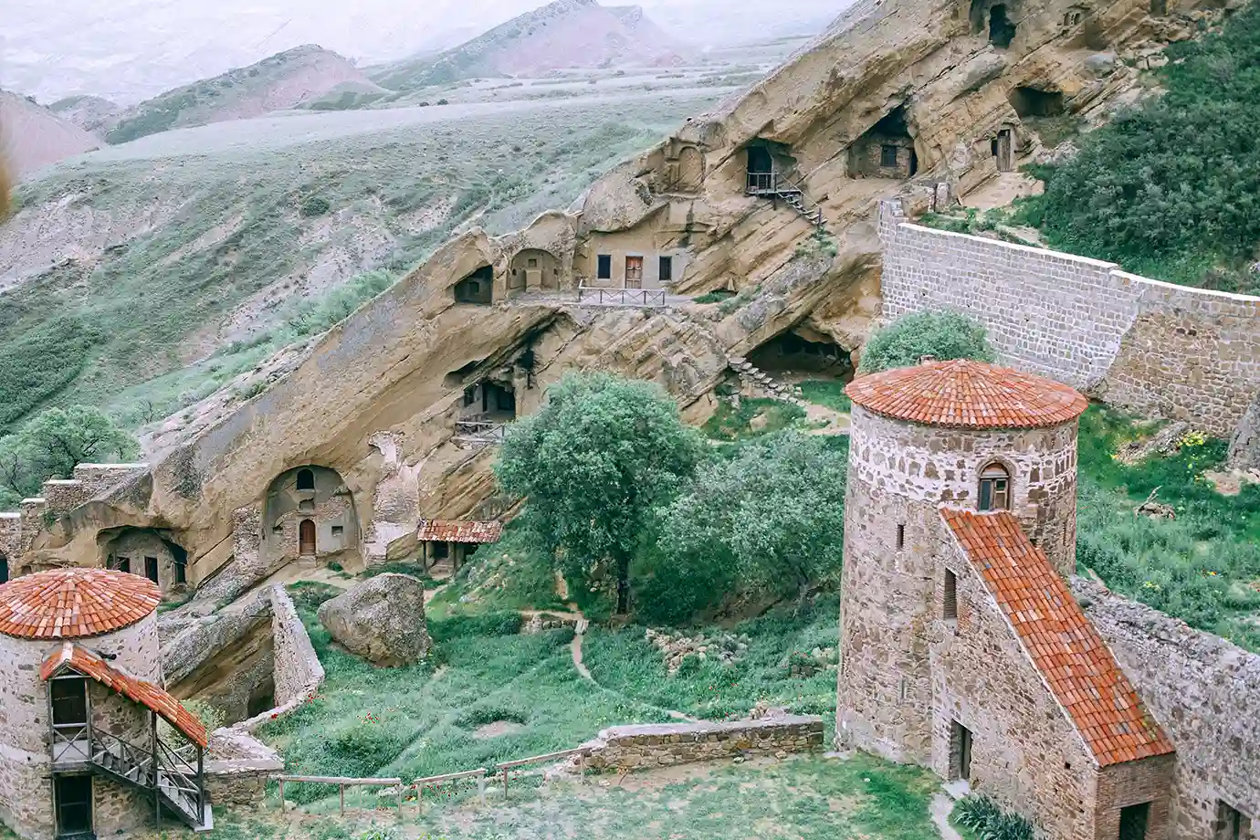 A high-angle view of the David Gareja cave monastery complex carved into a cliffside with stone towers and red-tiled roofs, highlighting unique Places to Visit in Georgia.