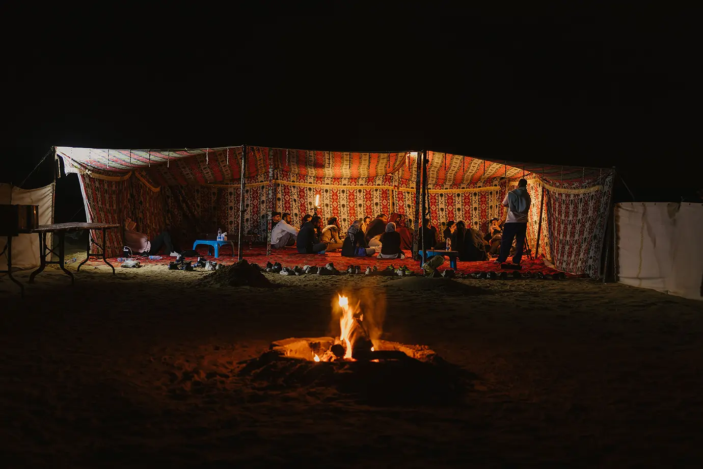 Travelers gathered inside a carpeted open-sided Bedouin tent around a crackling campfire during a Dubai Desert Safari.