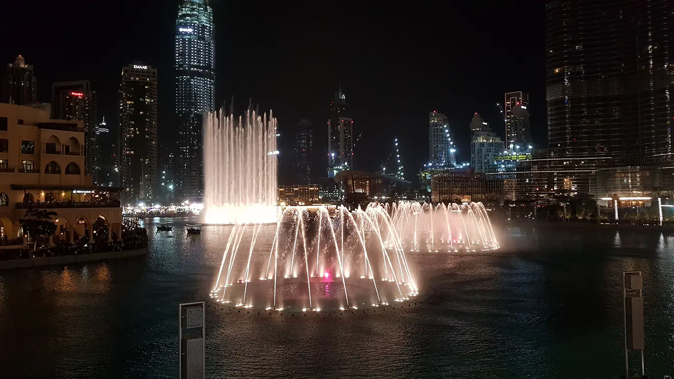 Illuminated water jets performing during the evening Dubai Fountain show surrounded by glowing skyscrapers, a popular highlight of Things to Do in Dubai.