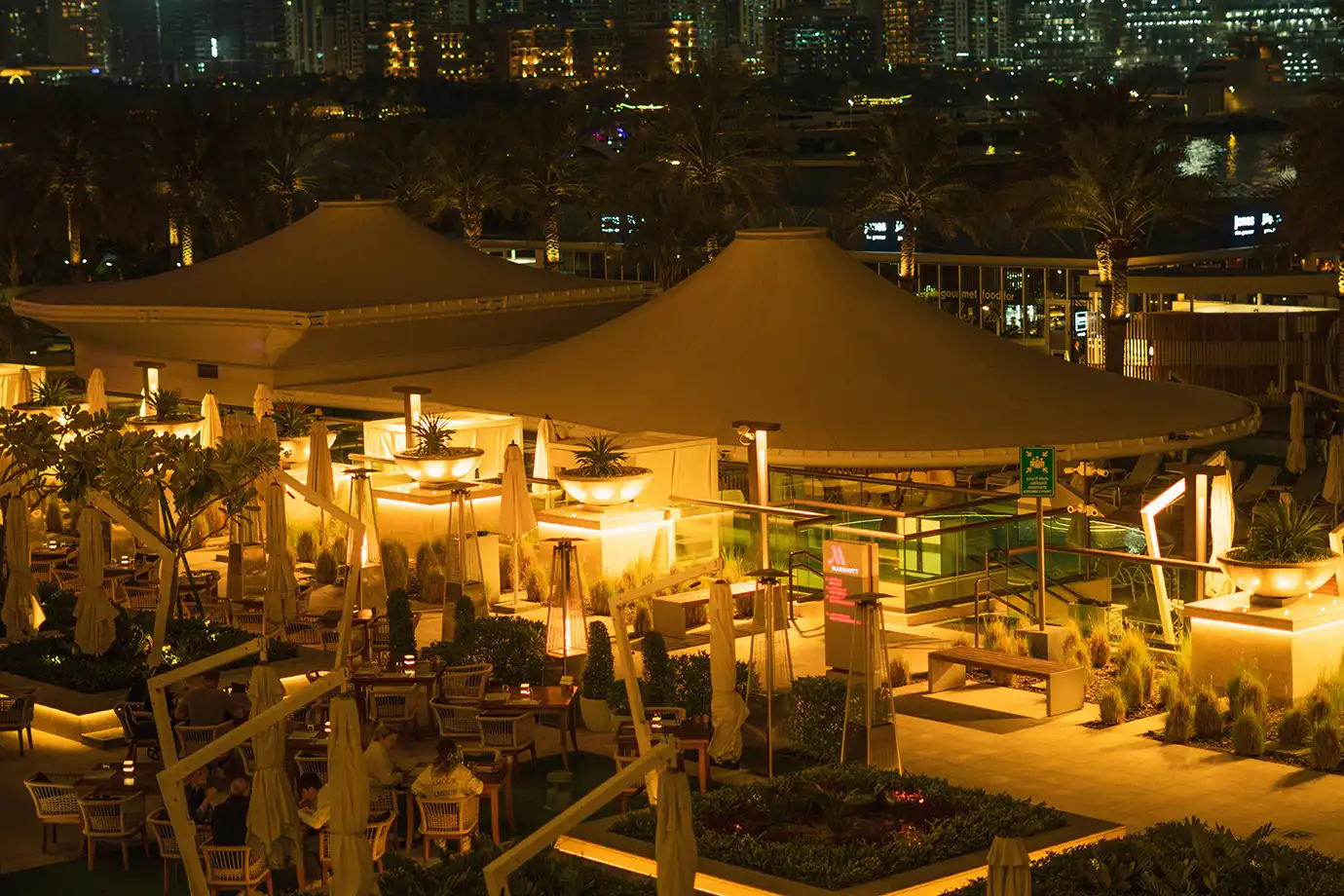 Guests dining at an elegantly lit outdoor restaurant patio under tented awnings at night, featured in Best Time to Visit Dubai.