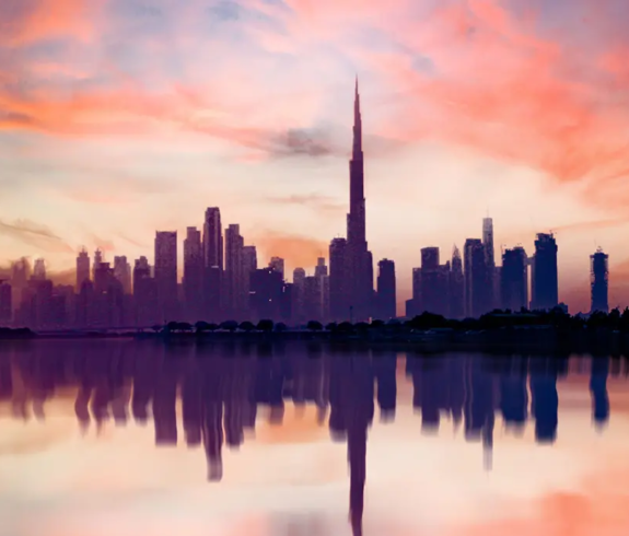 Silhouetted skyscrapers including the towering Burj Khalifa reflecting in calm waters under a vibrant pink and orange sunset sky, featured in Best Time to Visit Dubai