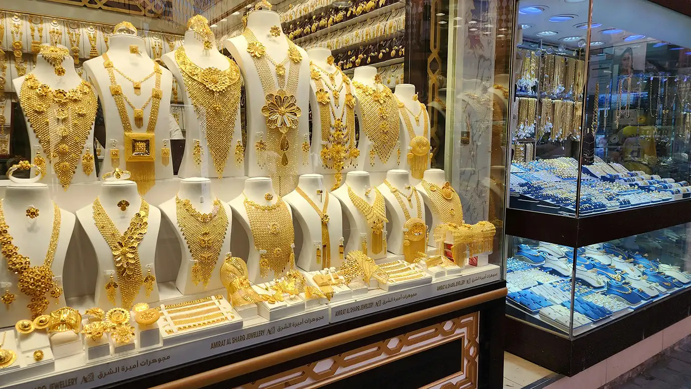 A glass storefront in Dubai filled with white mannequins wearing massive, intricately crafted gold necklaces, chest plates, and matching sets.