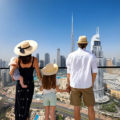 A family of four wearing sun hats standing on a balcony overlooking the Downtown skyline and iconic Burj Khalifa while exploring Dubai with Kids.