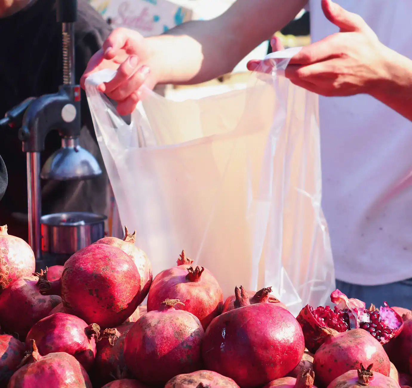 A mound of ruby-red pomegranates at a market stall with a vendor holding a bag next to a citrus juicer featured in a travel guide on When Is the Best Time to Visit Azerbaijan.