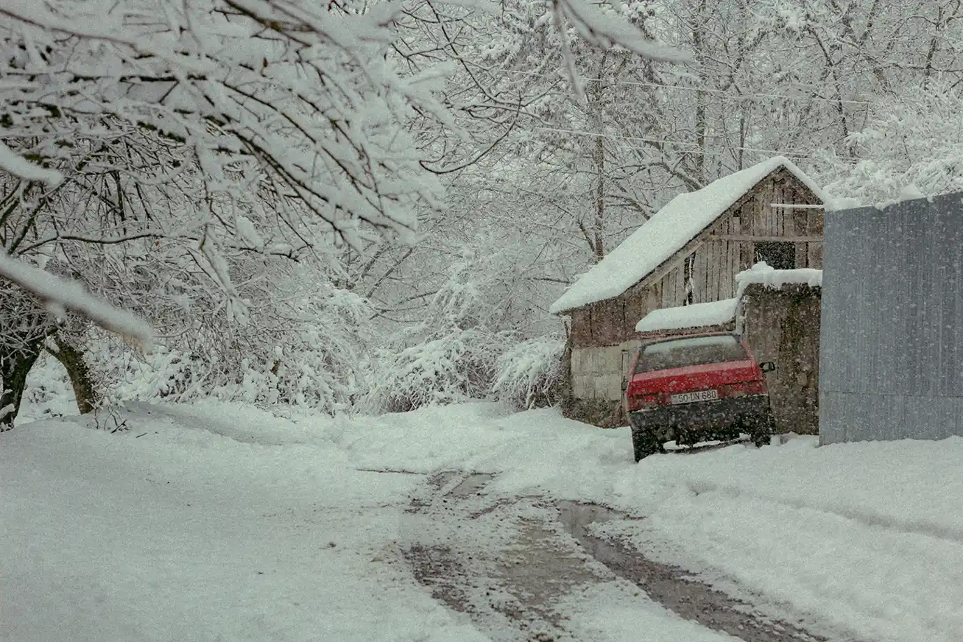 A red car parked next to a snow-capped wooden shed along a slushy, snow-draped rural road in Gabala featured in a travel guide on The Ultimate 7-Day Azerbaijan Itinerary.